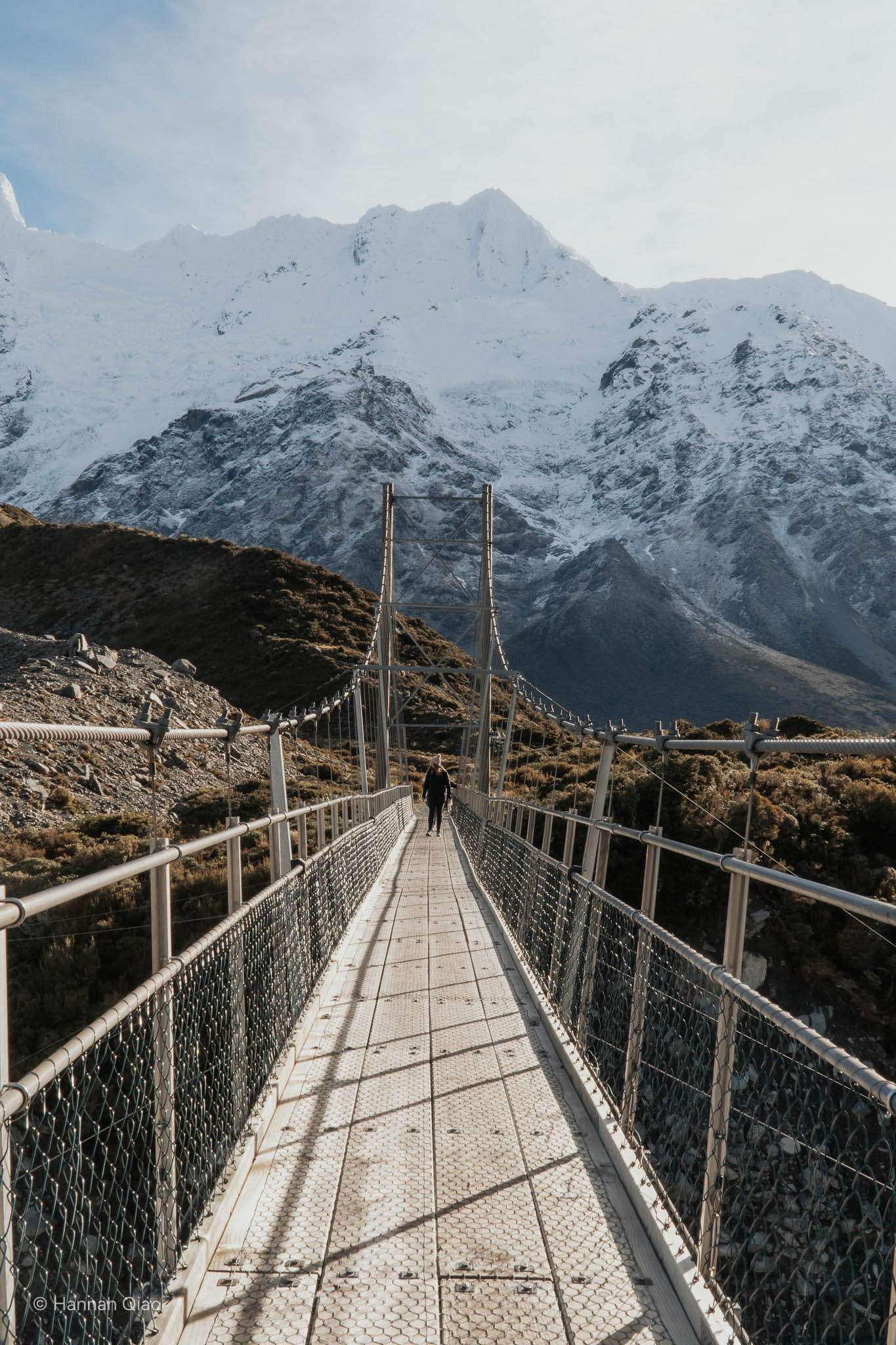 Photo of a woman on a bridge with a snowy mountain behind her