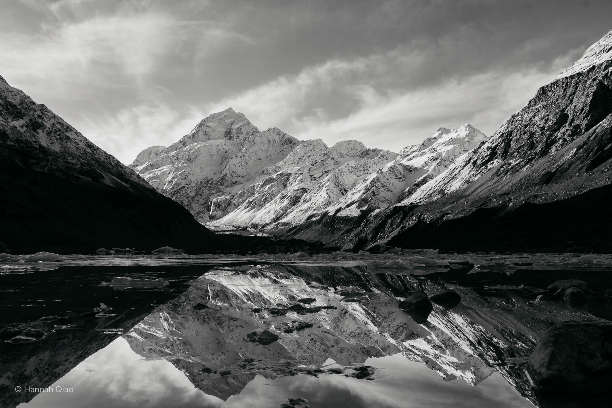 Black and white photo of a winter lake with snowy mountains around it