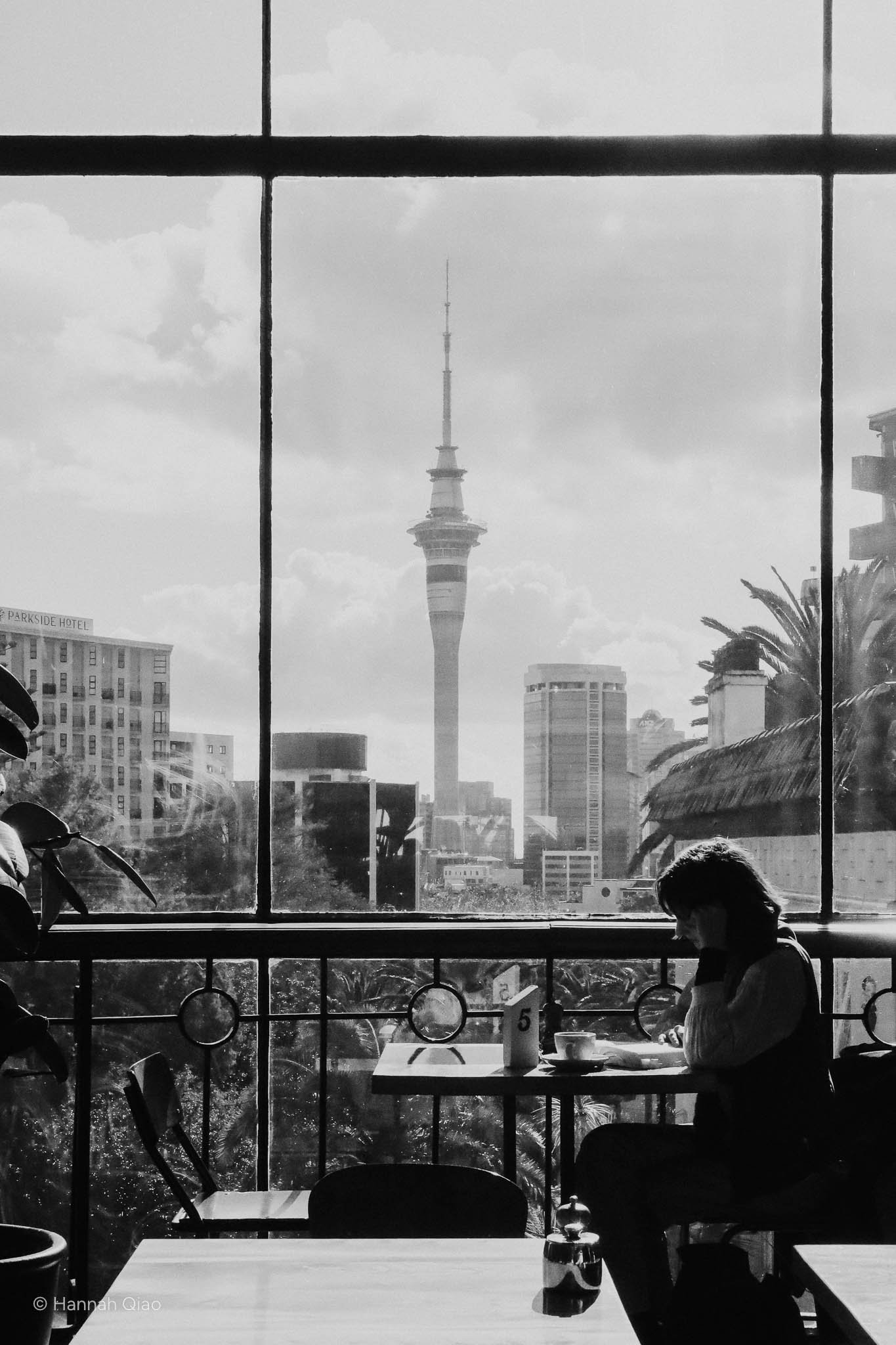 Photo of a woman sitting at a table with the Auckland sky tower behind her