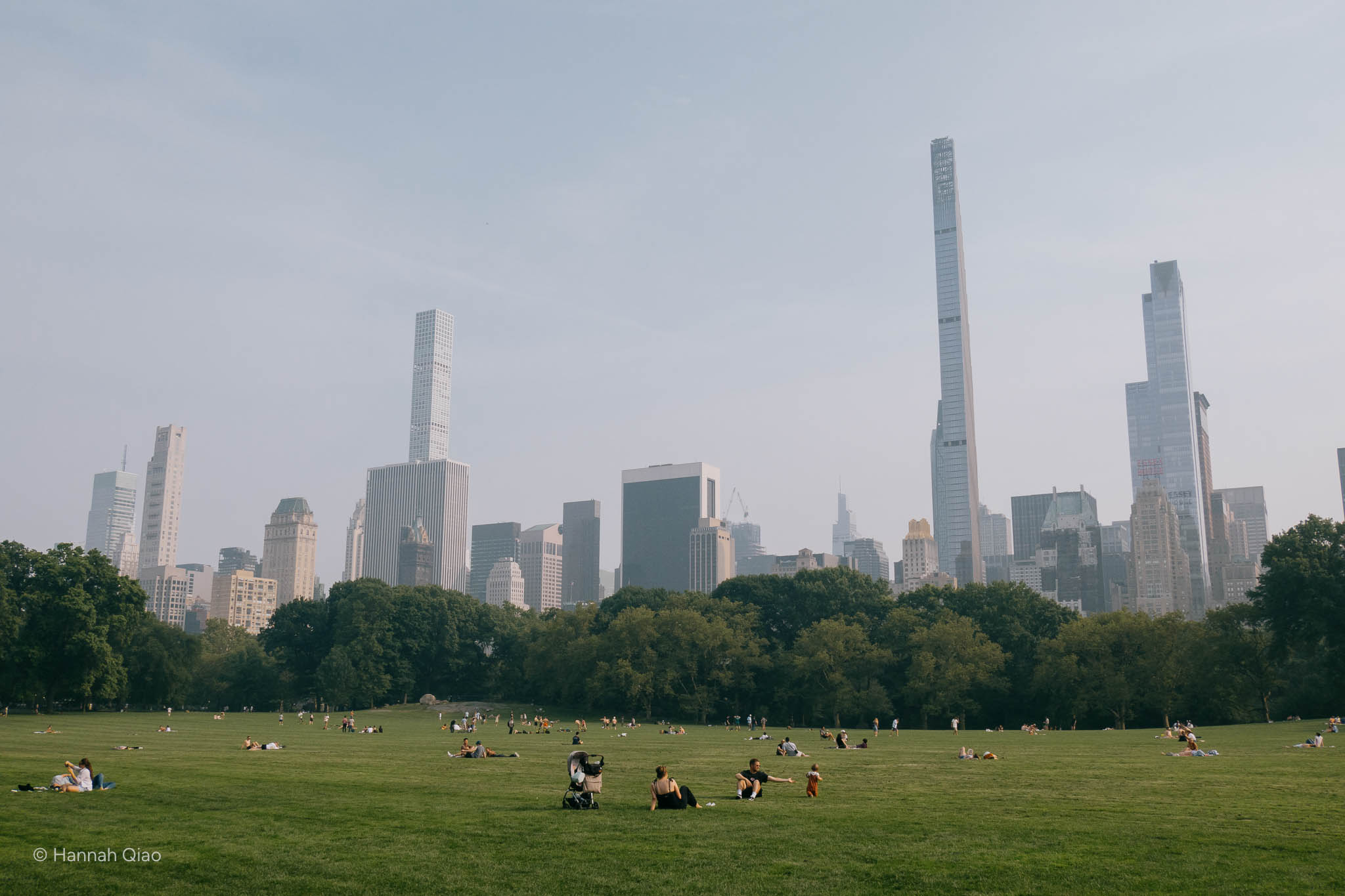 Photo of a park with people sitting on the grass and buildings in the background